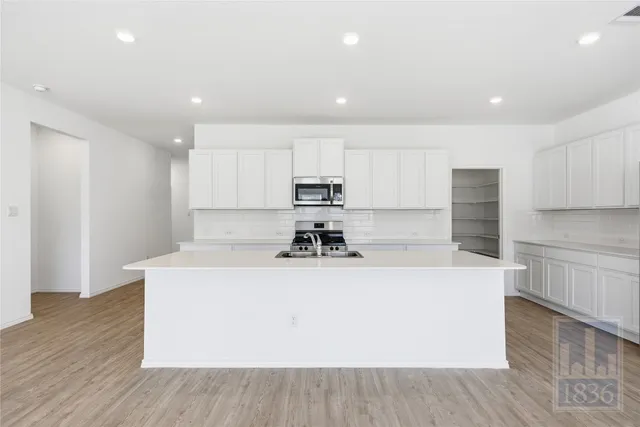 a view of a kitchen with kitchen island a sink wooden floor and a stove
