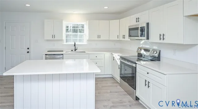 a kitchen with stainless steel appliances a sink dishwasher stove refrigerator and white cabinets with wooden floor