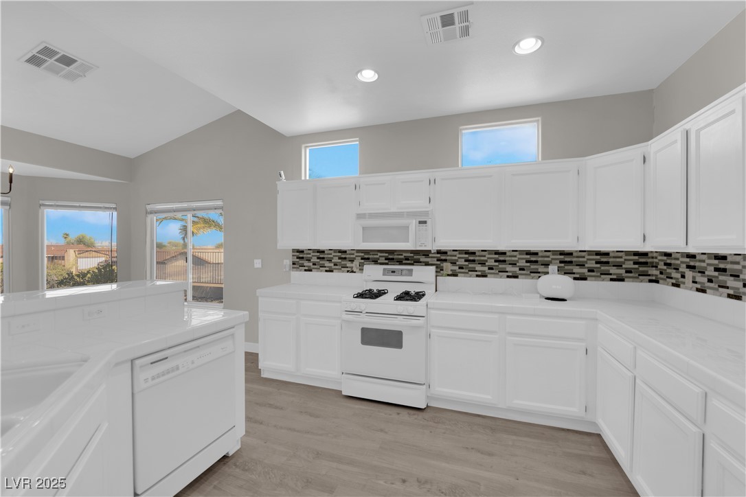 650 West Victory Road Henderson, NV 89015 - Photo 9 of 35 Kitchen with decorative backsplash, white appliances, light wood-type flooring, white cabinetry, and vaulted ceiling