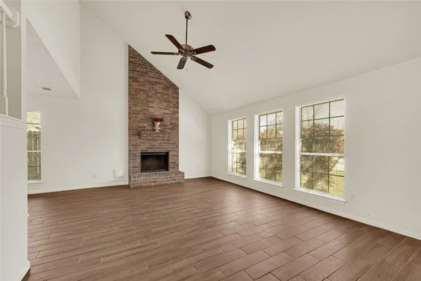 a view of an empty room with wooden floor fireplace and a window