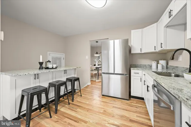 a kitchen with stainless steel appliances granite countertop a refrigerator a stove a sink dishwasher and white cabinets with wooden floor