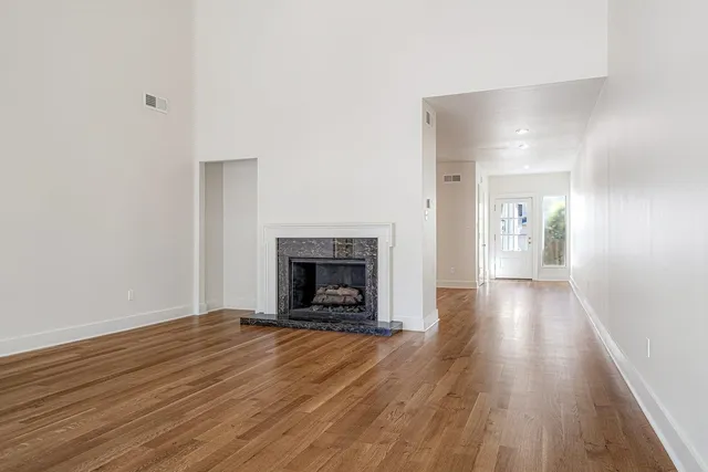 a view of an empty room with wooden floor and a fireplace