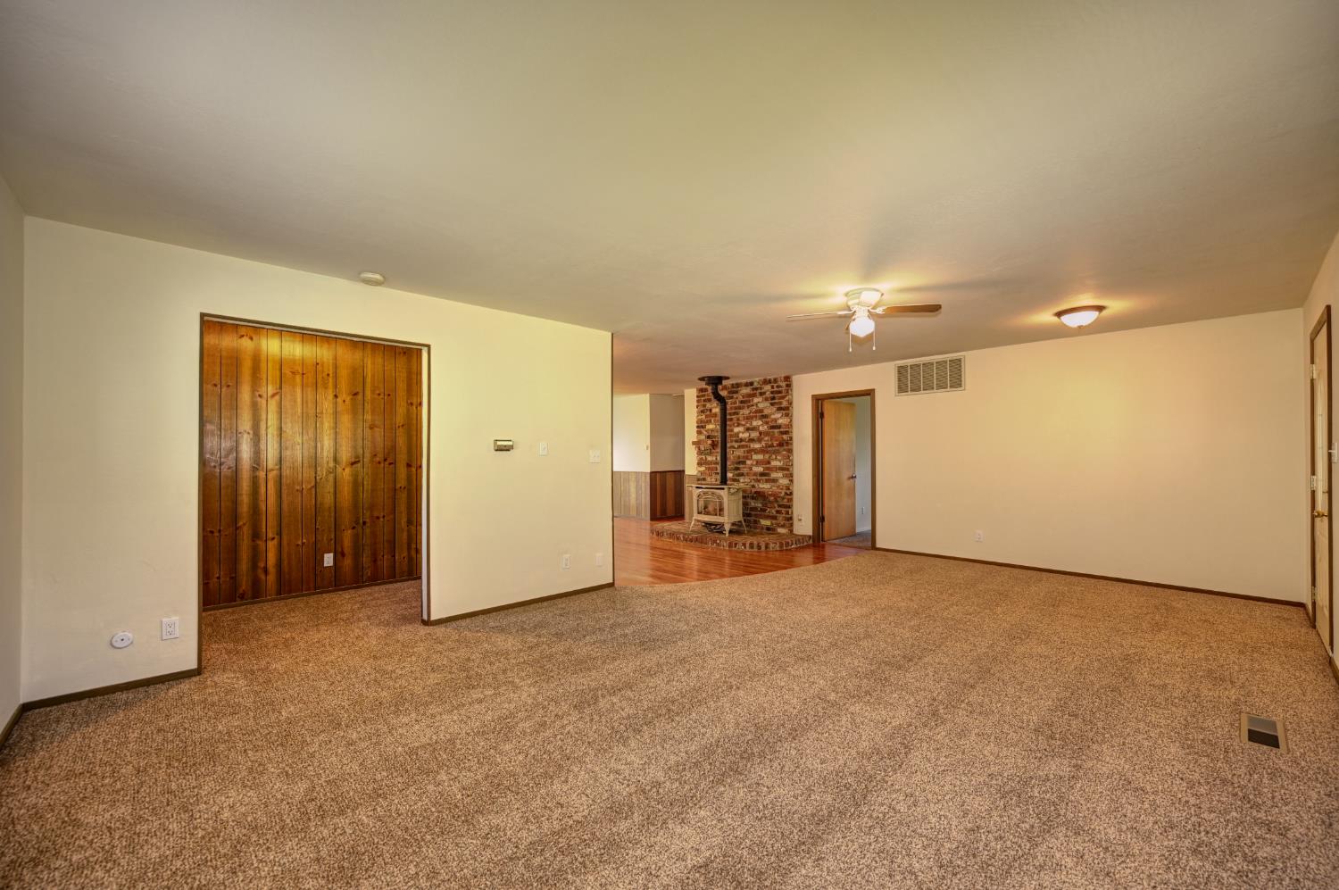 4541 Meadowbrook Road Garden Valley, CA 95633 - Photo 23 of 71 empty room featuring light colored carpet, a wood stove, and a ceiling fan