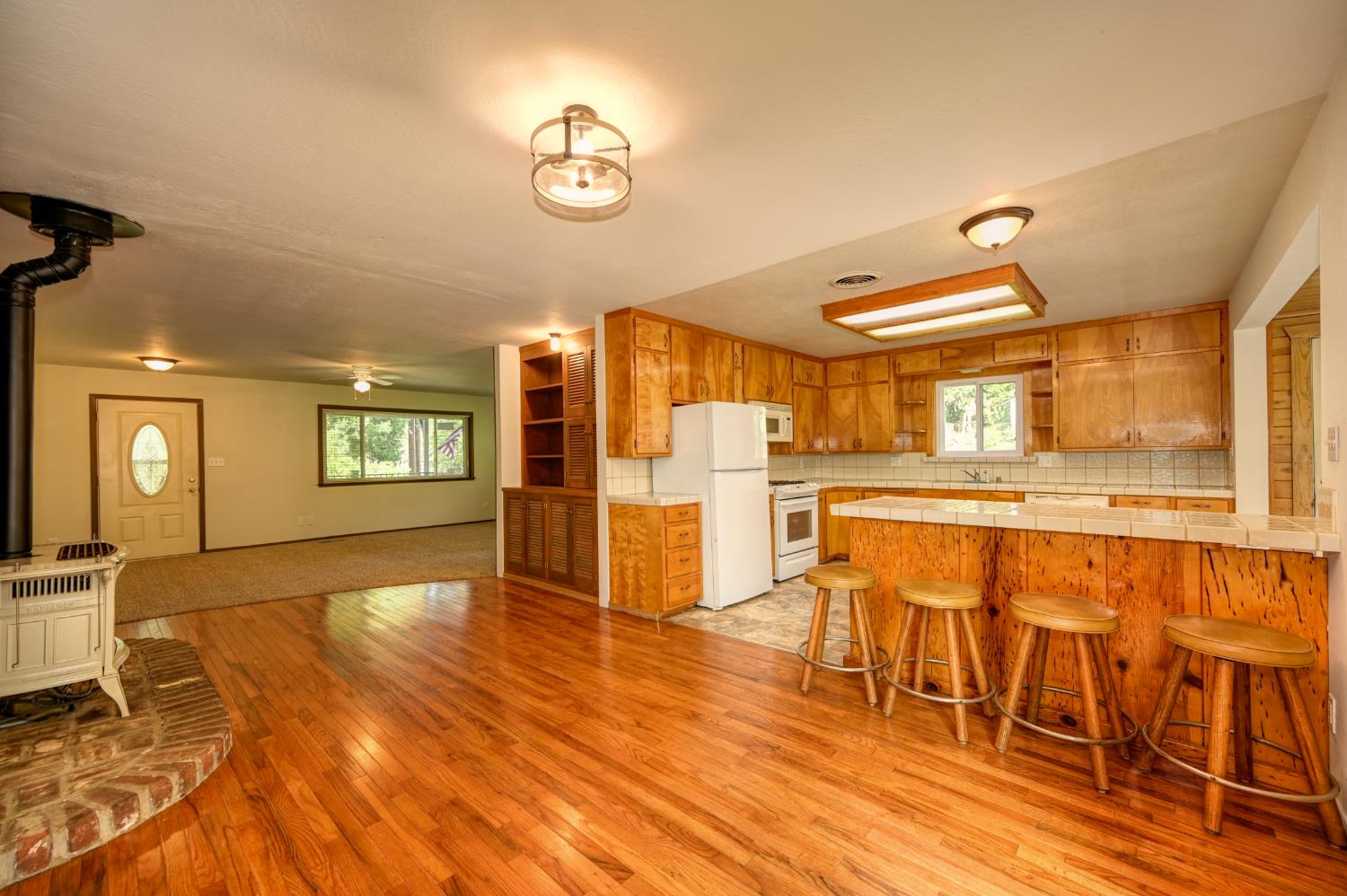 4541 Meadowbrook Road Garden Valley, CA 95633 - Photo 29 of 71 kitchen with a wood stove, tile counters, white appliances, open shelves, and a kitchen bar