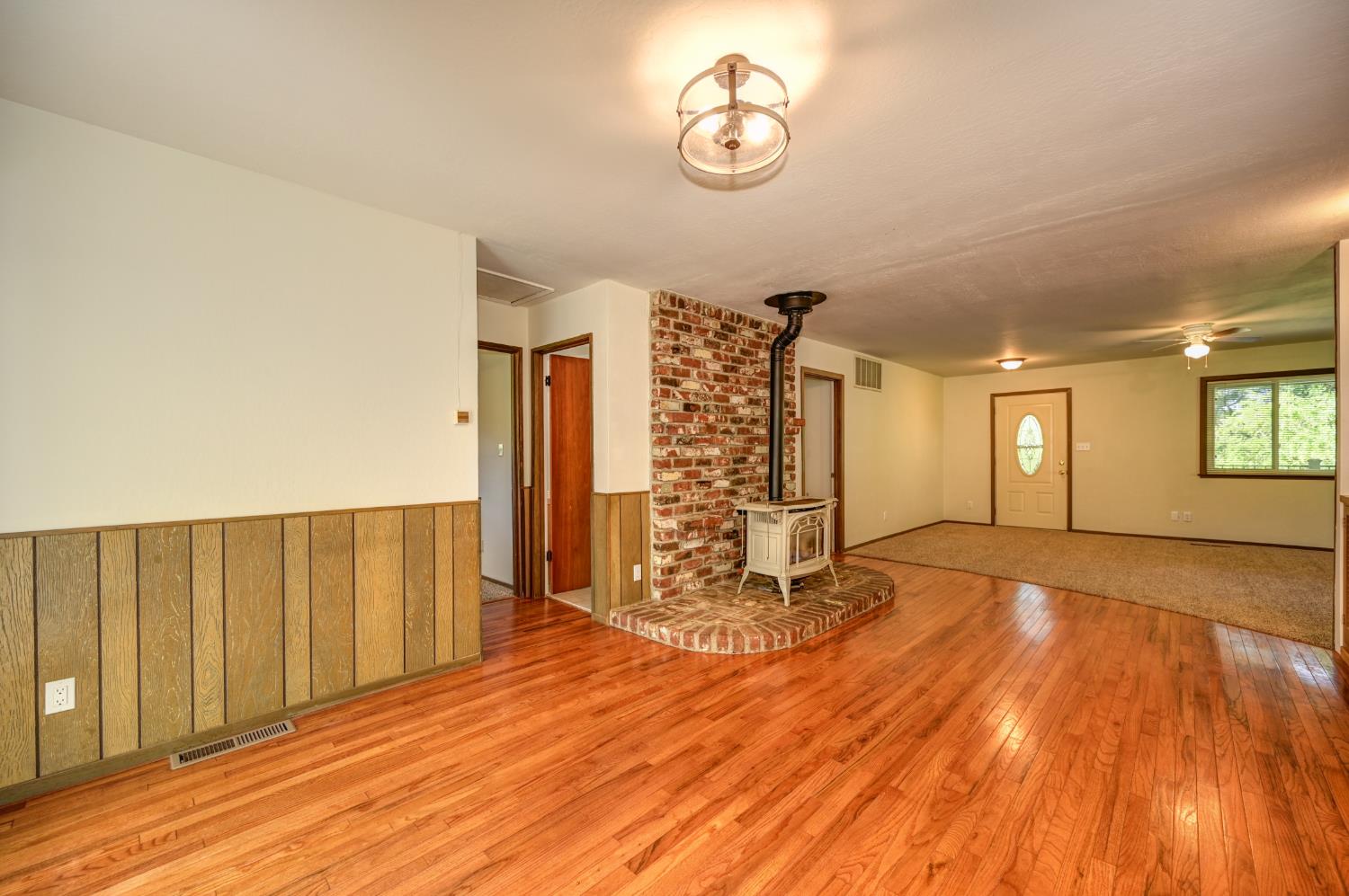 4541 Meadowbrook Road Garden Valley, CA 95633 - Photo 31 of 71 unfurnished living room featuring wood-type flooring, a wood stove, ceiling fan, wood walls, and a wainscoted wall