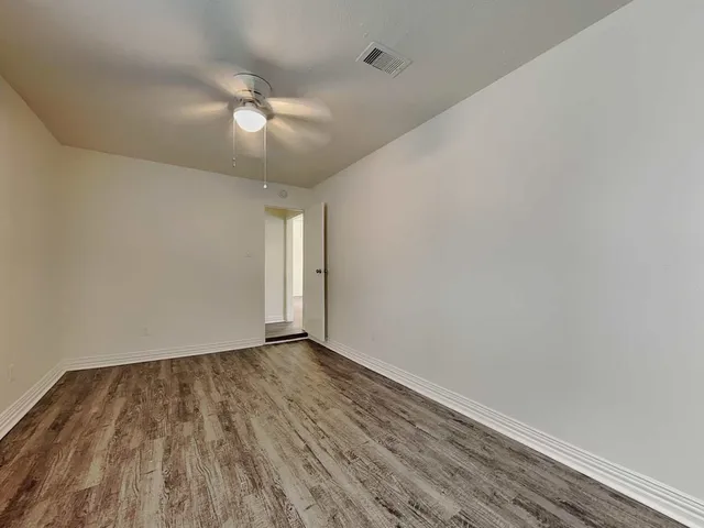 a view of an empty room with wooden floor and a ceiling fan