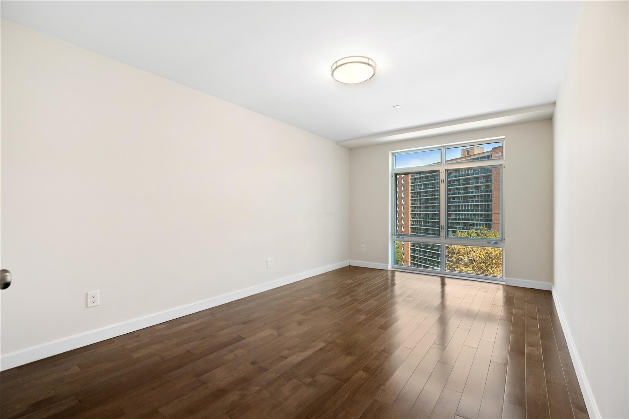 9745 63rd Drive, Unit 7A Queens, NY 11374 - Photo 14 of 20 a view of an empty room with wooden floor and a window