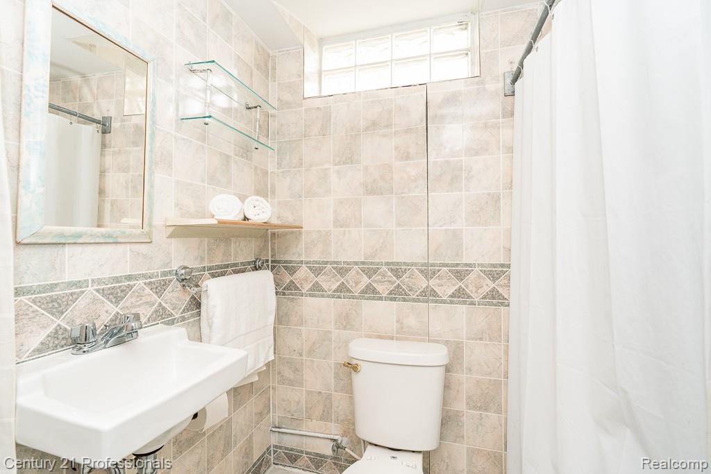 304 Highland Avenue Rochester, MI 48307 - Photo 19 of 30 Bathroom featuring extensive floor-to-ceiling tilework, a decorative tile border, a wall-mounted sink with chrome fixtures, and a glass block window for natural light