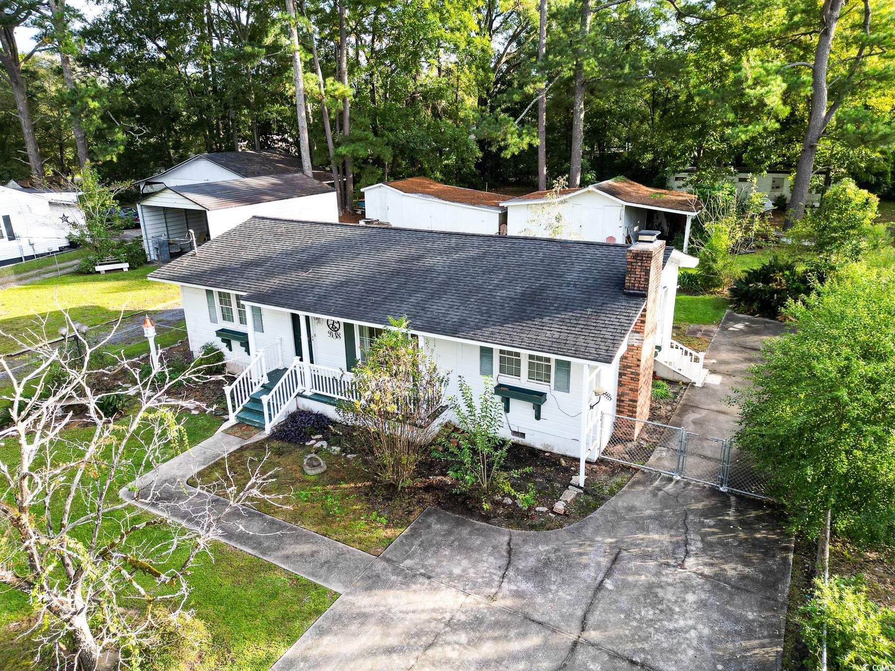 Ranch-style home with a gate, a shingled roof, a chimney, view of wooded area, and covered porch