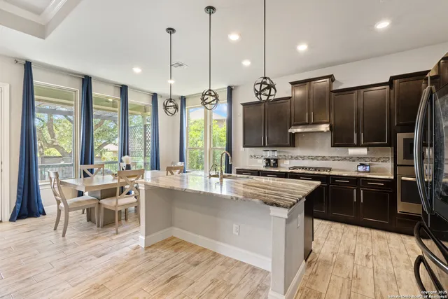 a kitchen with stainless steel appliances kitchen island granite countertop a stove a refrigerator a sink a dining table and chairs with wooden floor