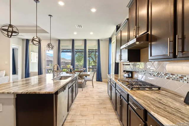 a large kitchen with granite countertop a sink counter top space a stove and a wooden floor