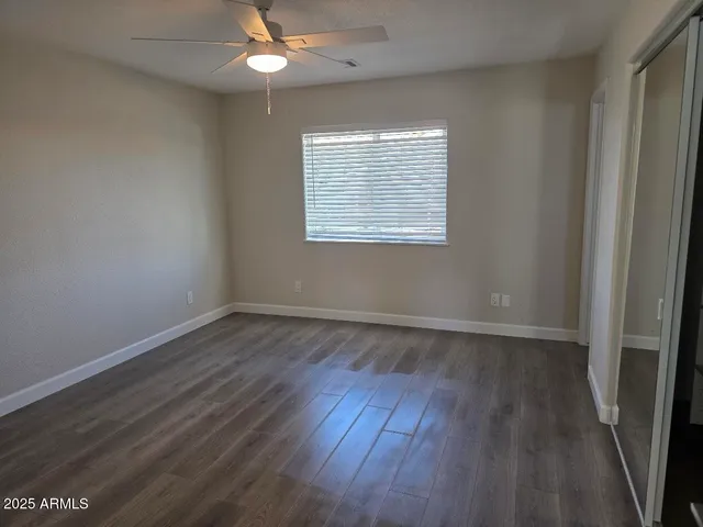 an empty room with wooden floor a ceiling fan and windows