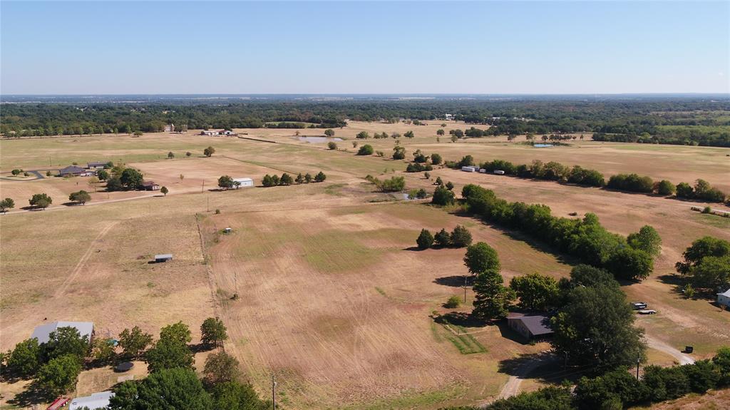 Expansive rural landscape featuring scattered trees, open fields, and distant structures