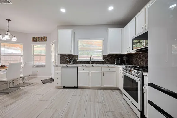 a kitchen with granite countertop a stove top oven a sink dishwasher and white cabinets with wooden floor