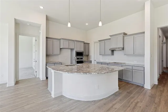 a kitchen with stainless steel appliances granite countertop a sink a stove a refrigerator and island with wooden floor