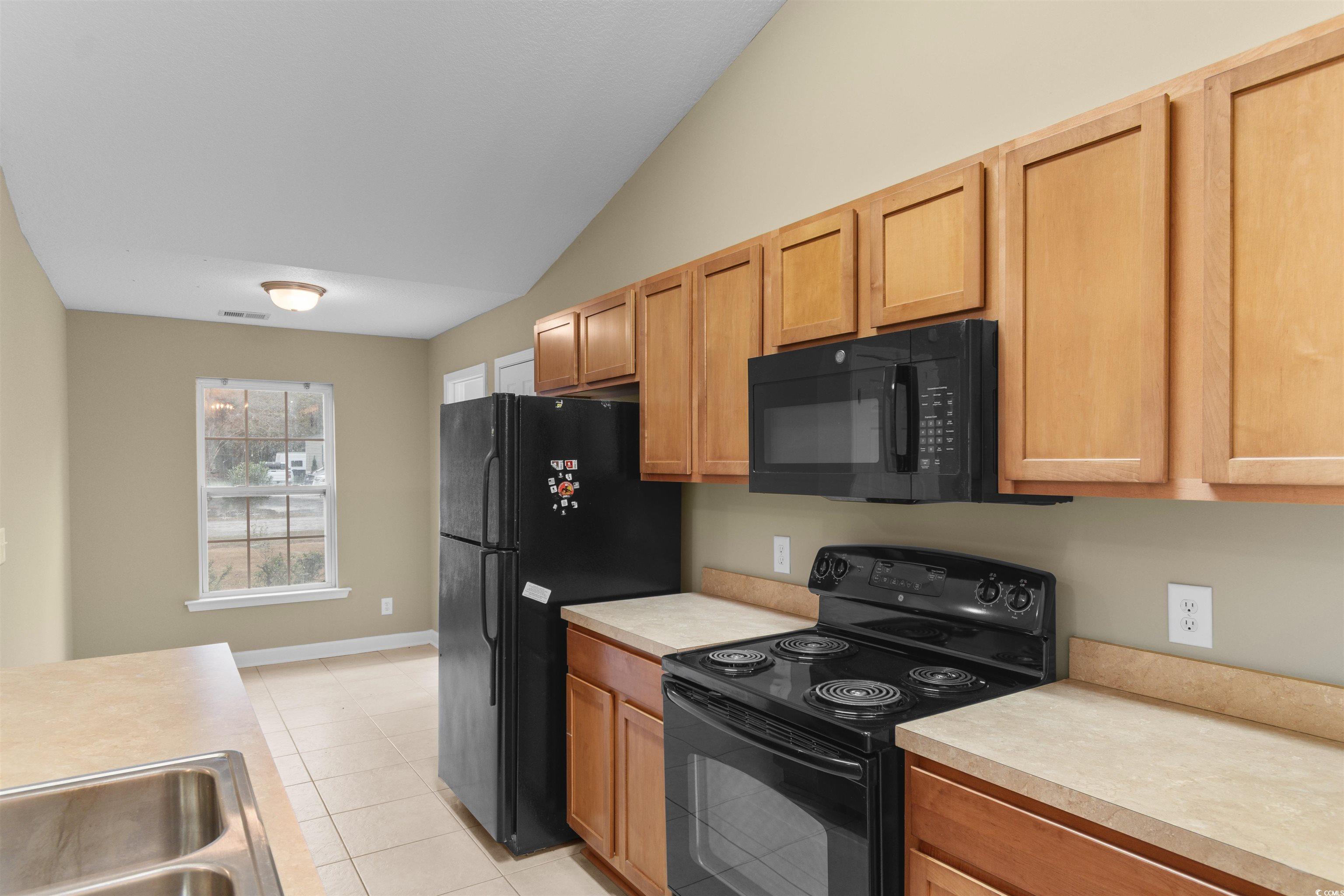 85 Graham Road Georgetown, SC 29440 - Photo 7 of 39 Kitchen featuring black appliances, light countertops, light tile patterned floors, vaulted ceiling, and light brown cabinets