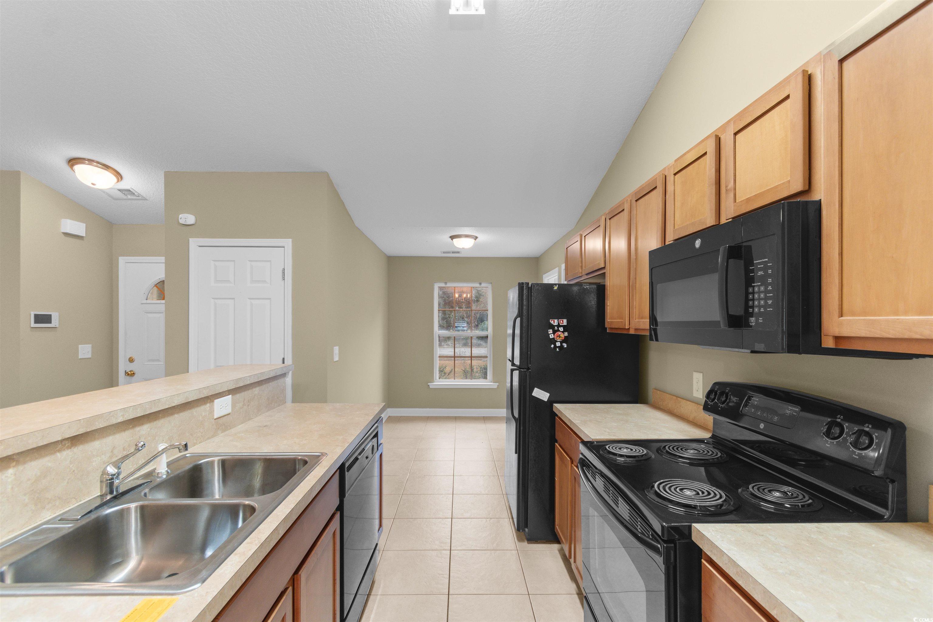 85 Graham Road Georgetown, SC 29440 - Photo 8 of 39 Kitchen with black appliances, light countertops, lofted ceiling, light tile patterned flooring, and light brown cabinetry