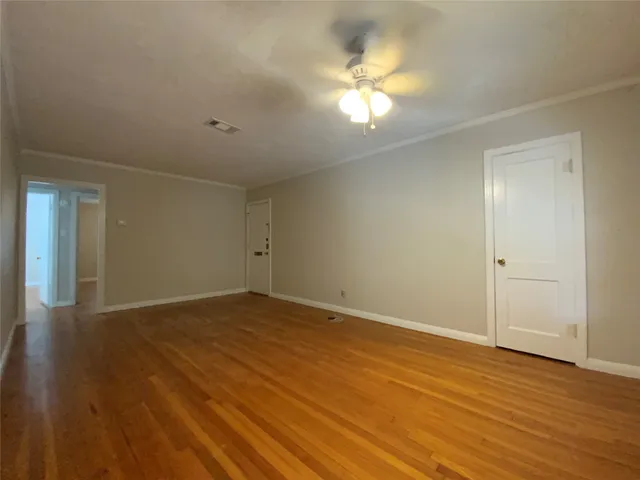a view of an empty room with wooden floor and a fan