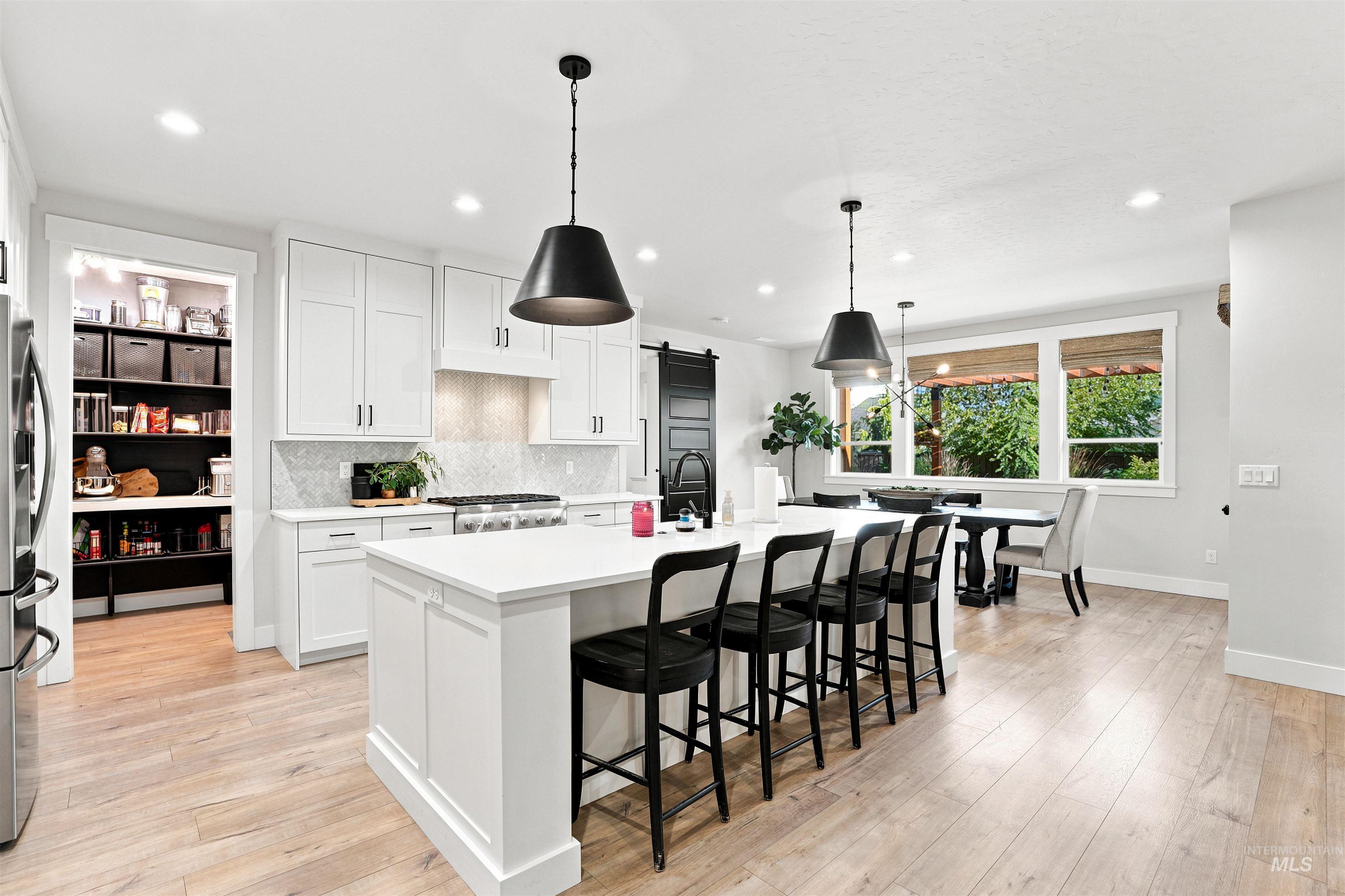 4323 West Ladle Rpds Drive Meridian, ID 83646 - Photo 8 of 49 Kitchen featuring an expansive center island with seating, white shaker cabinetry, light wood-finish flooring, a patterned backsplash, and a pantry with built-in shelving
