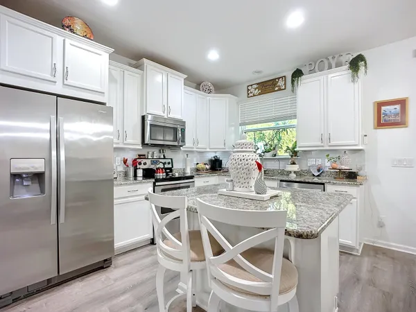 a kitchen with stainless steel appliances granite countertop a refrigerator a sink a stove a dining table and chairs