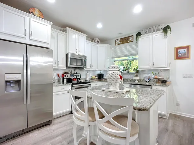 a kitchen with stainless steel appliances granite countertop a refrigerator a sink a stove a dining table and chairs