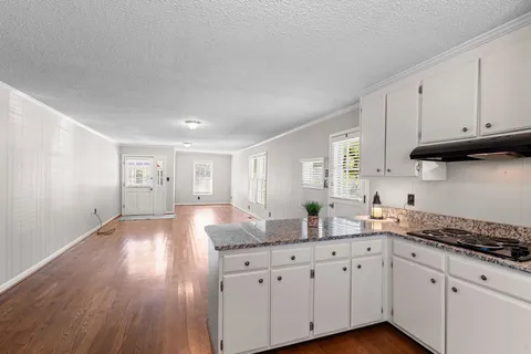 a kitchen with granite countertop wooden floors white cabinets and stainless steel appliances