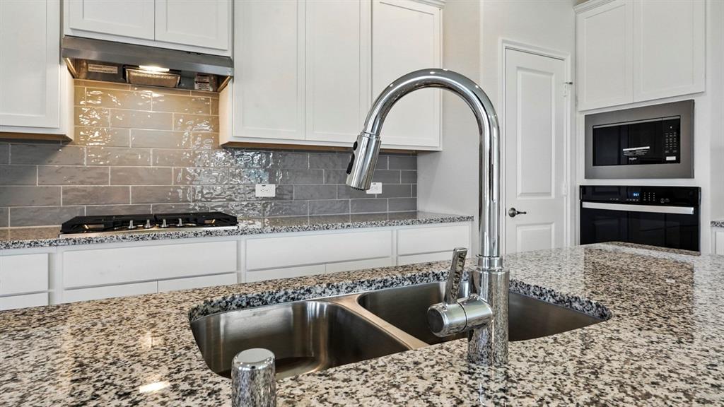4191 Waldron Trail Forney, TX 75126 - Photo 4 of 20 Kitchen featuring a double basin stainless steel sink with a high-arc faucet, granite countertops, white cabinetry, and a gray subway tile backsplash