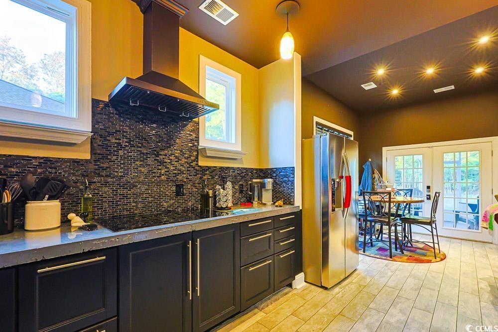 105 Rocko Drive Myrtle Beach, SC 29579 - Photo 3 of 38 Kitchen featuring backsplash, dark cabinetry, wall chimney exhaust hood, stainless steel refrigerator with ice dispenser, and hanging light fixtures