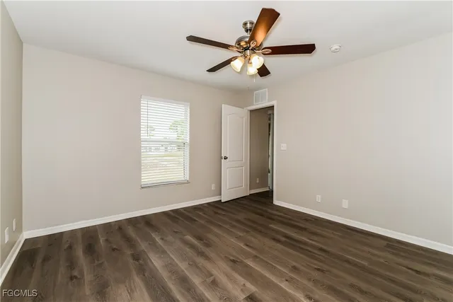 an empty room with wooden floor fan and windows
