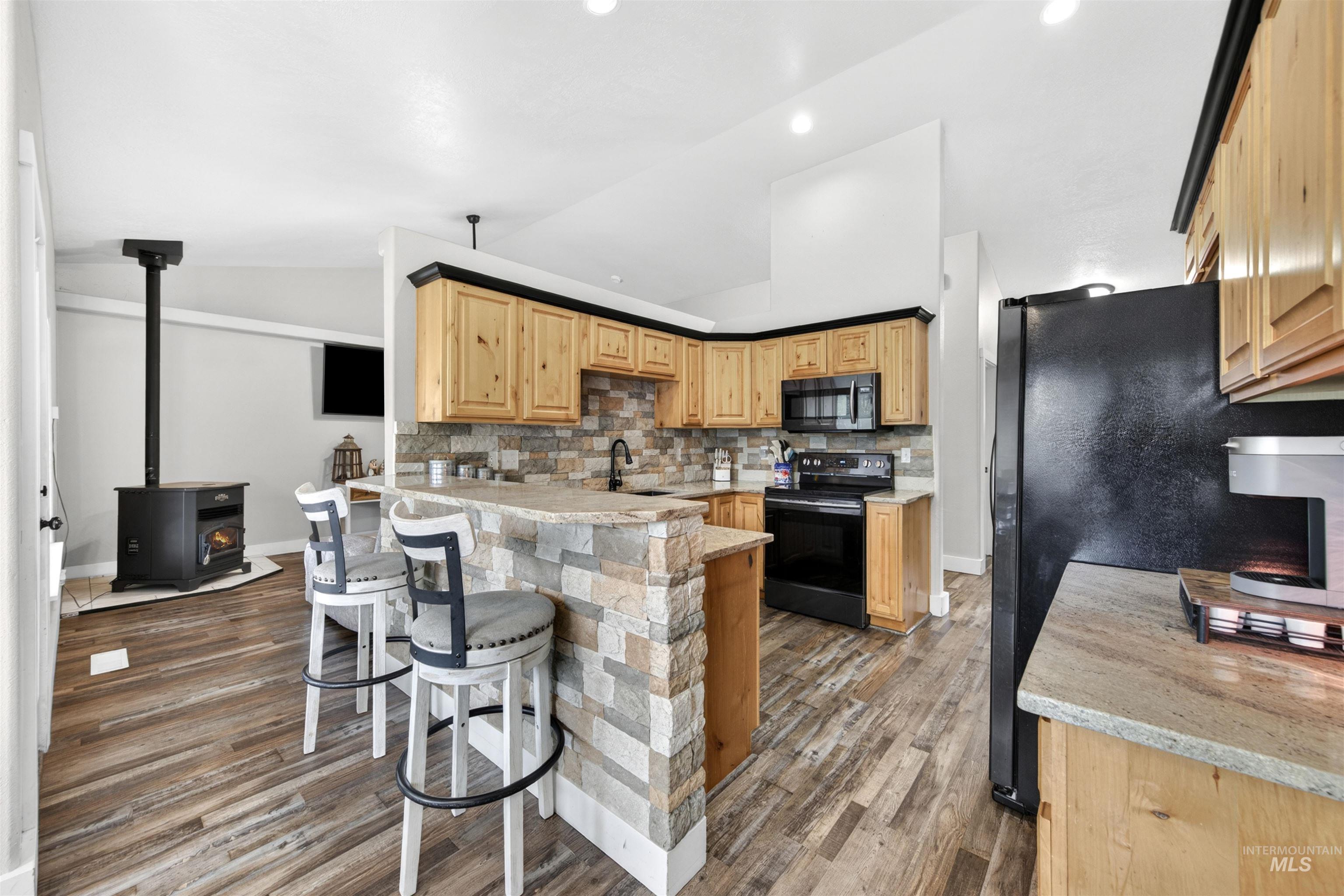 4 Round Up Circle Boise, ID 83716 - Photo 9 of 47 Kitchen featuring knotty wood cabinetry, stone-look backsplash, black appliances, and a breakfast bar with a stone-clad base