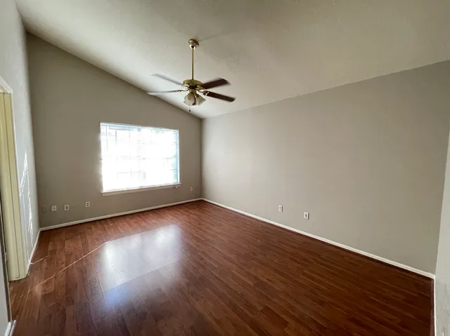 an empty room with wooden floor chandelier fan and windows