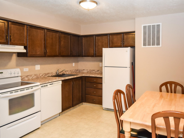 240 East 400 North, Unit 26 Logan, UT 84321 - Photo 5 of 10 Kitchen featuring white appliances, dark wood finish cabinets, light countertops, light floors, and a textured ceiling
