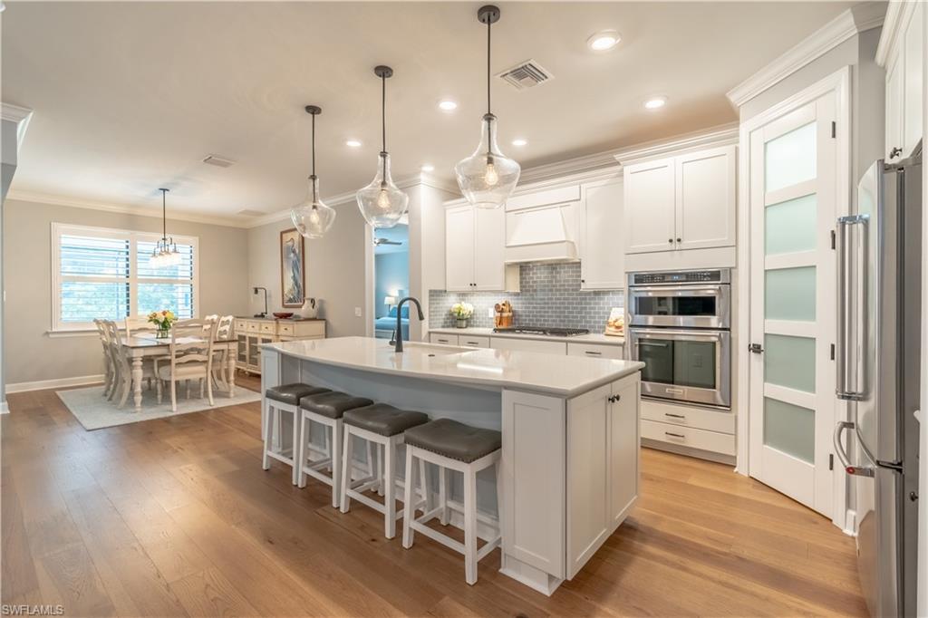 6848 Winding Cypress Drive Naples, FL 34114 - Photo 3 of 47 a kitchen with stainless steel appliances granite countertop a stove a sink dishwasher a refrigerator and white cabinets with wooden floor