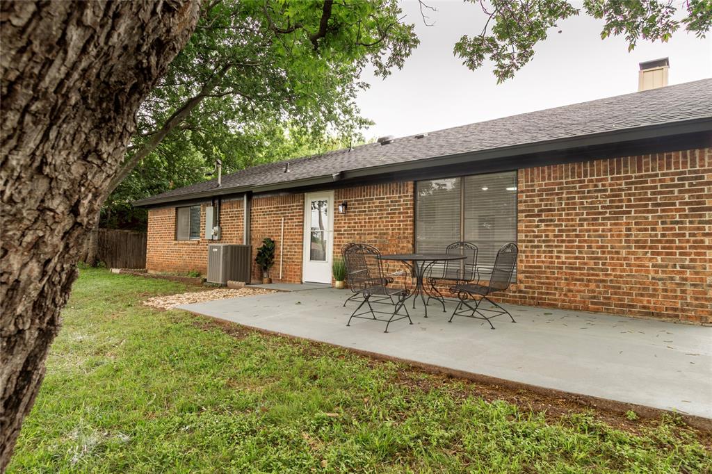 1205 Augusta Road Benbrook, TX 76126 - Photo 19 of 21 Backyard featuring a red brick exterior, a grey concrete patio, and a dark shingle roof