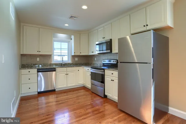 a kitchen with white cabinets white stainless steel appliances and wooden floors