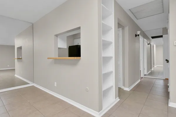 an empty room with windows and view of kitchen