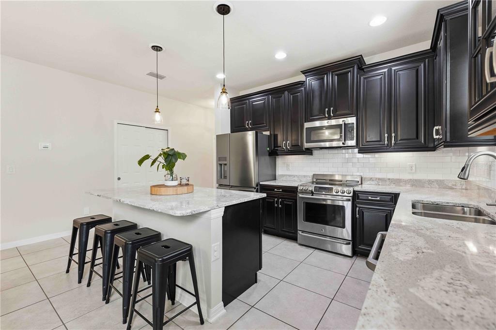 10920 79th Street East Parrish, FL 34219 - Photo 7 of 73 a kitchen with stainless steel appliances granite countertop a stove top oven a sink a stove a dining table and chairs