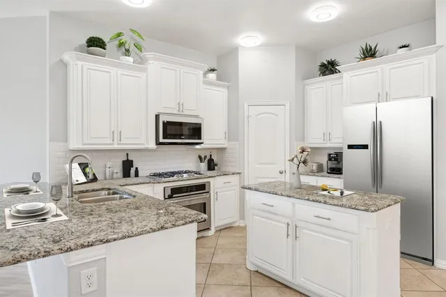 a kitchen with stainless steel appliances granite countertop a sink stove refrigerator and white cabinets with wooden floor