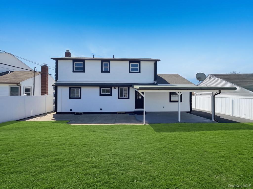 61 Cheshire Road Bethpage, NY 11714 - Photo 3 of 25 Expansive green lawn with a white two-story exterior featuring dark trim, a covered patio, and a privacy fence