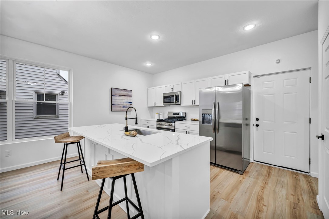3734 Pennington Road Cleveland, OH 44120 - Photo 11 of 45 Kitchen featuring white cabinetry, stainless steel appliances, a kitchen bar, a center island with sink, and light wood-type flooring
