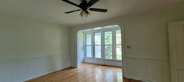 an empty room with wooden floor chandelier fan and windows