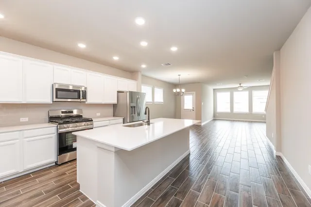 a view of a kitchen with kitchen island a sink wooden floor and stainless steel appliances