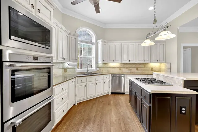 a kitchen with stainless steel appliances kitchen island granite countertop a stove top oven a sink dishwasher and white cabinets with wooden floor