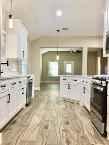 a large white kitchen with kitchen island a sink stainless steel appliances and cabinets