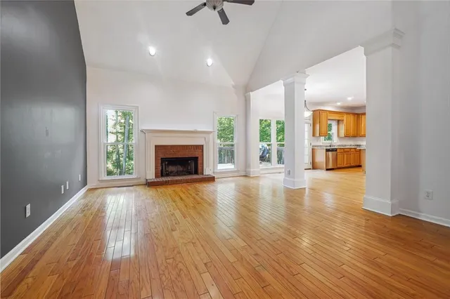 an empty room with wooden floor a ceiling fan a fireplace and windows
