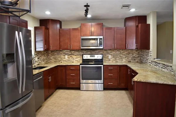 a kitchen with stainless steel appliances granite countertop wooden cabinets a refrigerator and a sink
