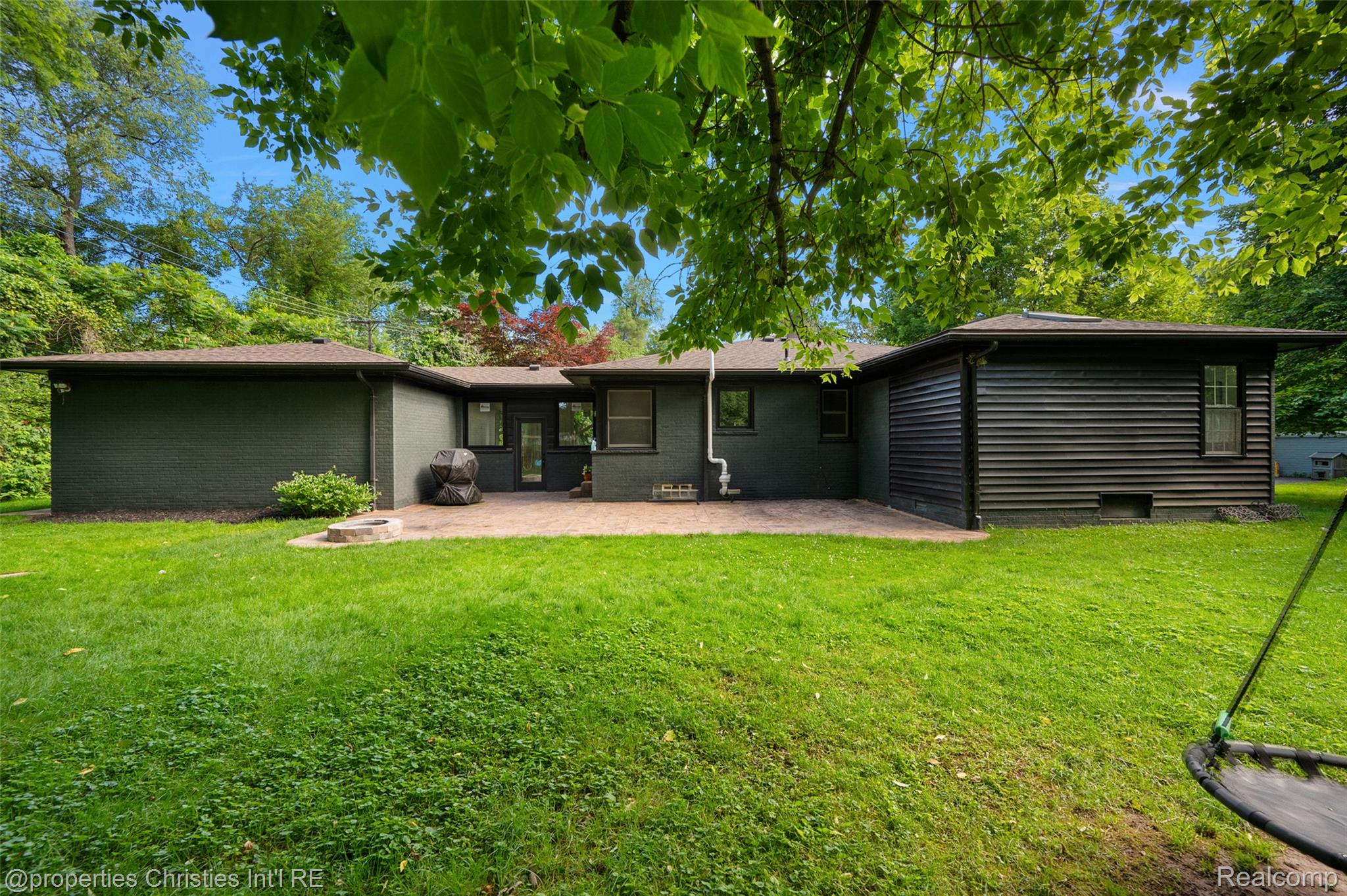 27331 Gardenway Road Franklin, MI 48025 - Photo 9 of 65 Expansive grassy backyard featuring a paved patio, a built-in fire pit, and dark exterior siding
