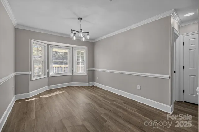 an empty room with wooden floor chandelier and windows