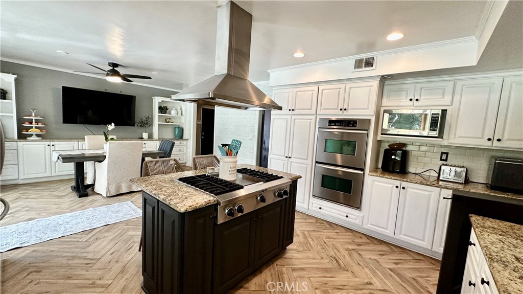 19559 Tulsa Street Porter Ranch, CA 91326 - Photo 19 of 55 a kitchen with stainless steel appliances kitchen island granite countertop a stove top oven a sink dishwasher a dining table and chairs with wooden floor