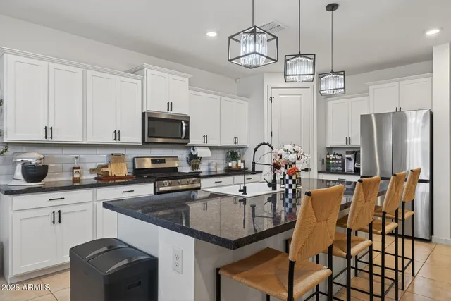 a kitchen with stainless steel appliances granite countertop a stove top oven a sink a refrigerator a stove a dining table and chairs